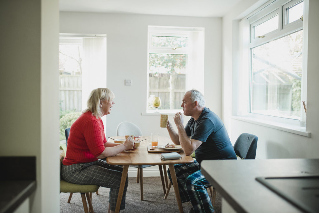 Mature couple are having breakfast together at the dining table in their home.