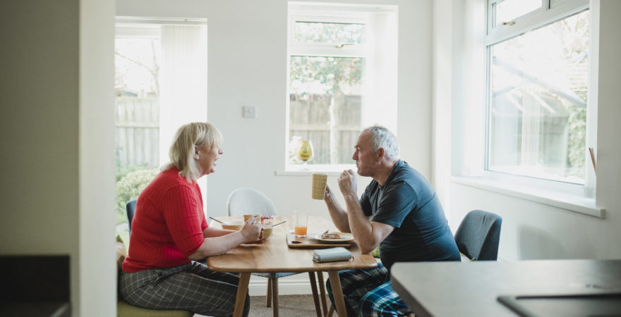 Mature couple are having breakfast together at the dining table in their home.