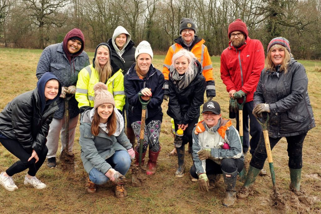 Group of Hinckley & Rugby Building Society colleagues huddled together smiling after planting trees whilst holding tools.