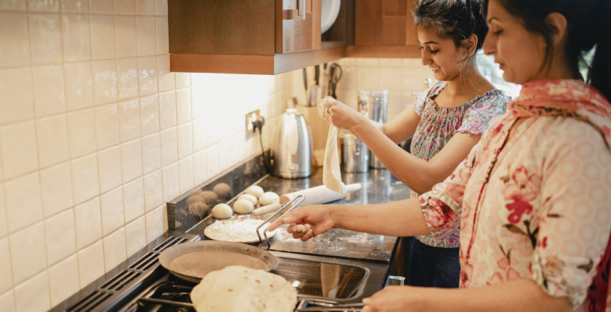 Mother and daughter cooking chapattis on the stove.