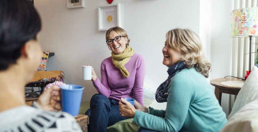 Mature women friends and sisters sitting together in a living room in Cornwall talking together.