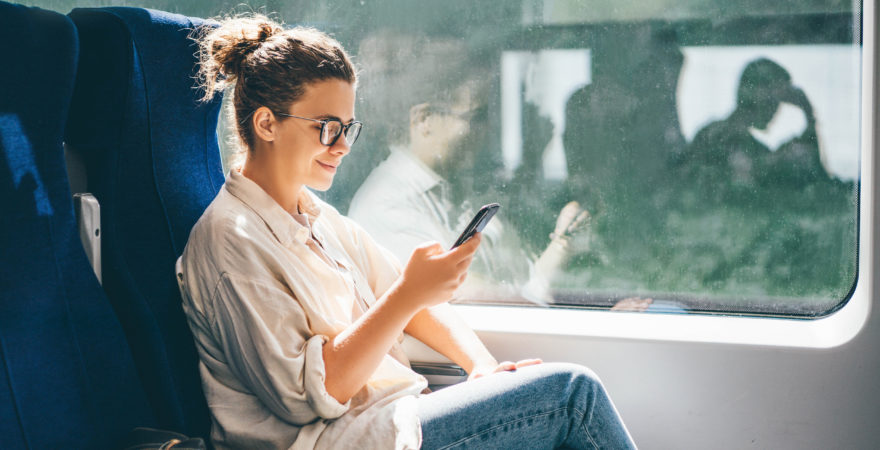 Young woman traveling by train and using phone.