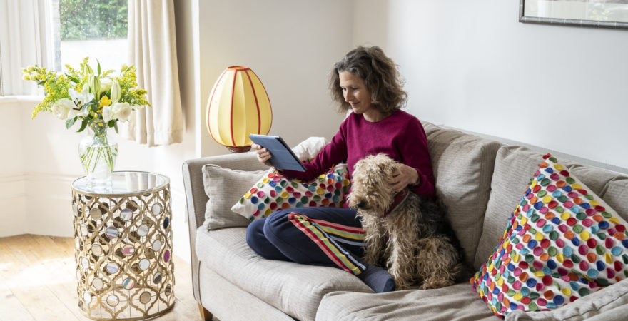 Woman relaxing on sofa at home with dog reading digital tablet.