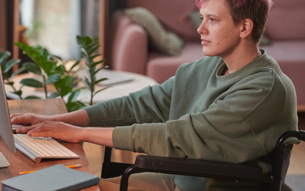 Image of a woman with short hair and a green top working on a laptop.