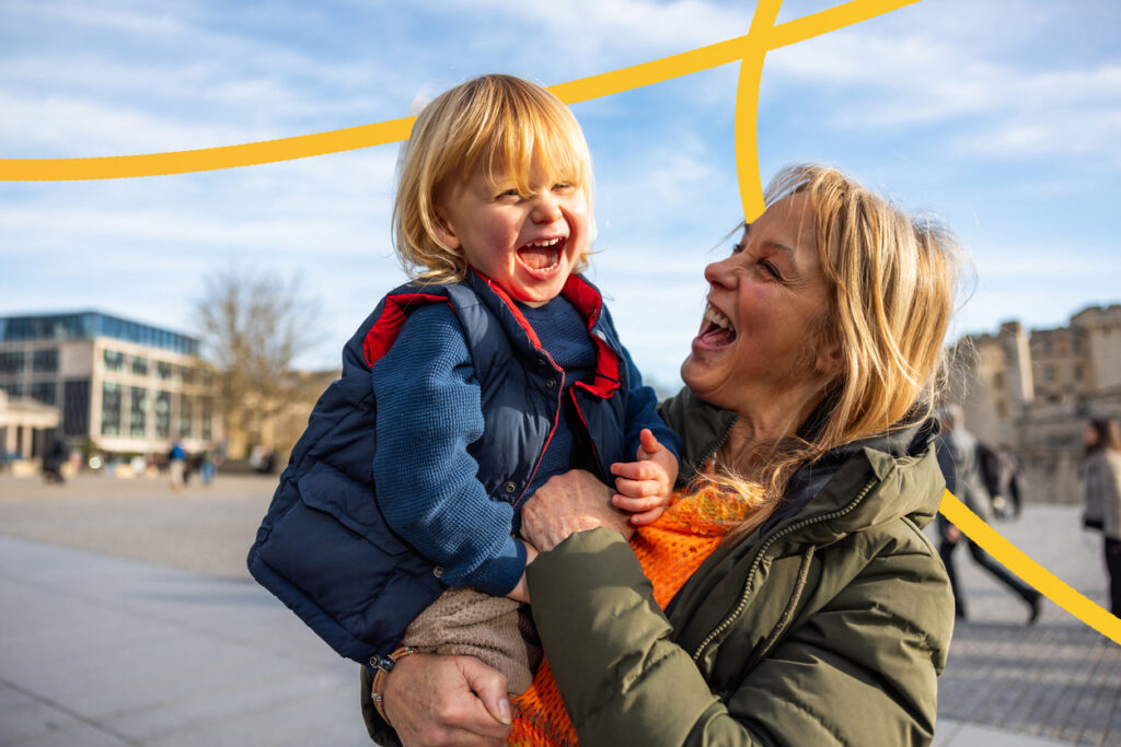 Grandmother holding her grandson, both laughing and enjoying a sunny day in the square near the Tower of London, showing family love and connection