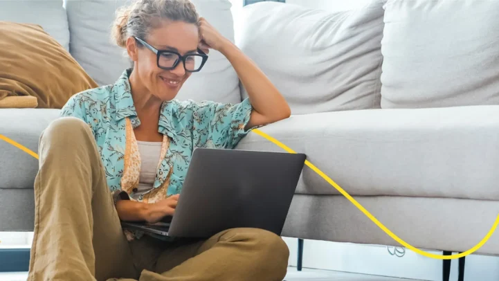 A woman sat on the floor with a laptop on her lap, looking at fixed rate bonds.