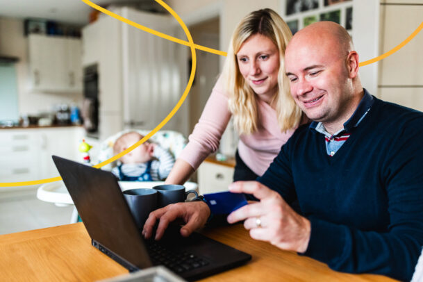A young couple looking at a computer and discussing cash ISA transfers. They are both smiling at the screen.