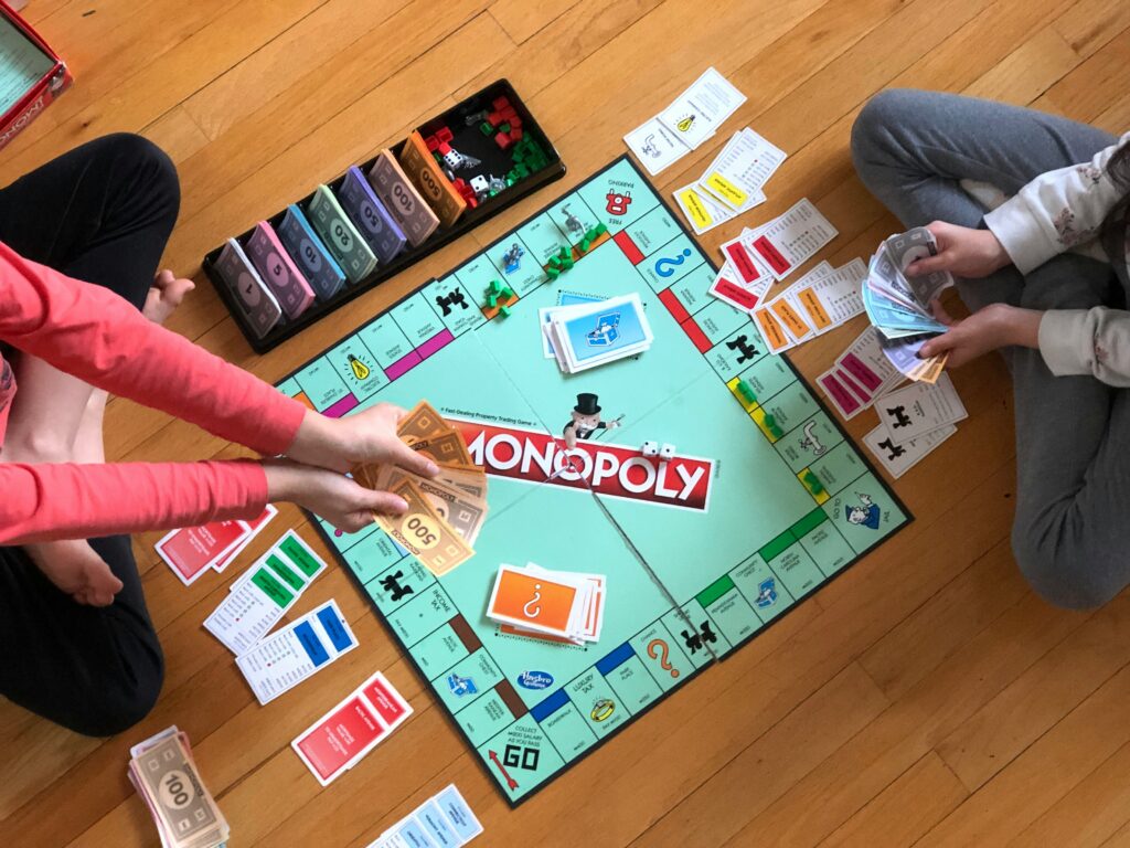 Two children sitting on the floor and playing the board game Monopoly.